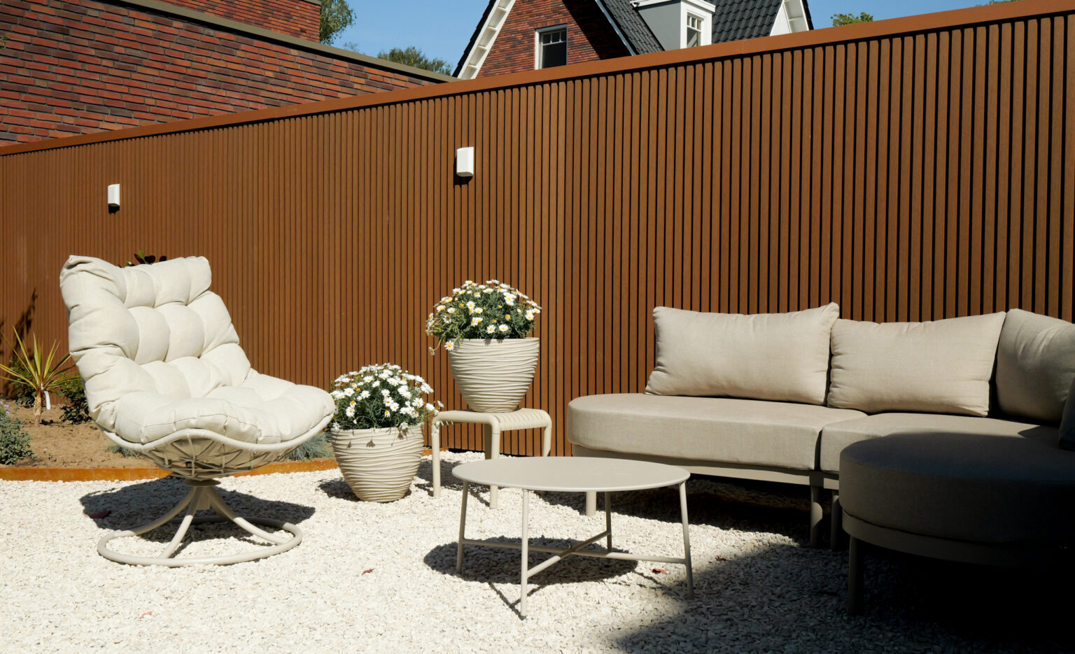 Luxe loungehoek met moderne houtcomposiet schutting, licht tuinmeubilair, siergrind en onderhoudsvriendelijke tuin.